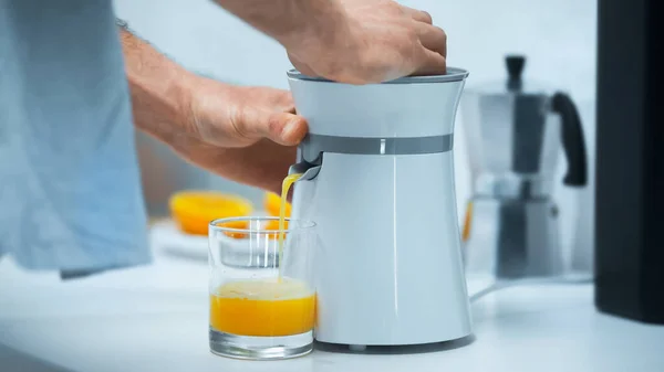 Vista recortada del hombre preparando jugo de naranja fresco para el desayuno en la cocina - foto de stock