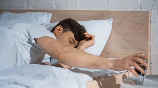 Homme couché au lit et éteignant réveil vintage le matin — Photo de stock