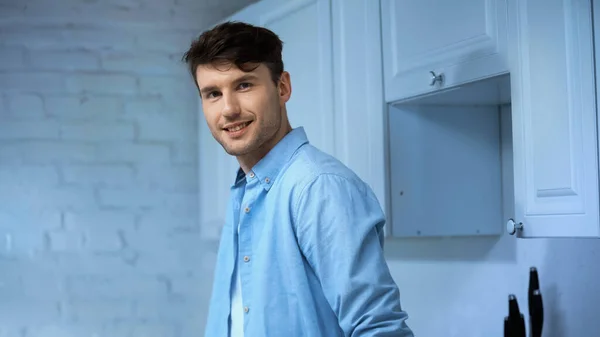 Веселий чоловік у блакитній сорочці дивиться на камеру на кухні — стокове фото