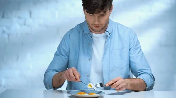 Homme avec fourchette et couteau manger des œufs frits pour le petit déjeuner — Photo de stock