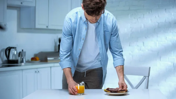 Mann deckt Küchentisch mit leckeren Toasts mit Marmelade und Orangensaft — Stockfoto