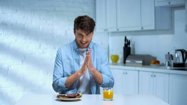 Pleased man rubbing hands near toasts with confiture and orange juice in kitchen — Stock Photo