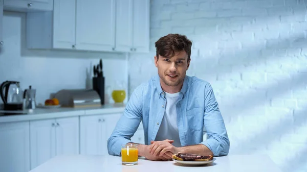 Man smiling at camera while sitting near toasts with jam and glass of orange juice — Stock Photo