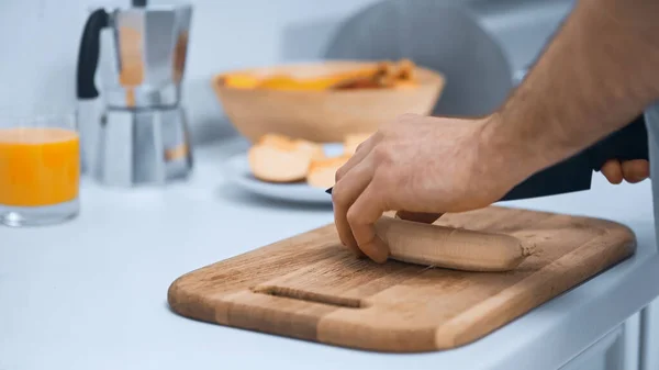 Vista recortada del hombre cortando plátano fresco mientras prepara el desayuno en la cocina - foto de stock