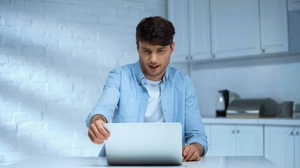 Homme en chemise bleue regardant ordinateur portable tout en travaillant dans la cuisine — Photo de stock