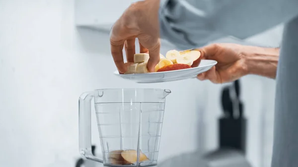 Vista recortada del hombre añadiendo manzana cortada y plátano en un tazón de licuadora — Stock Photo