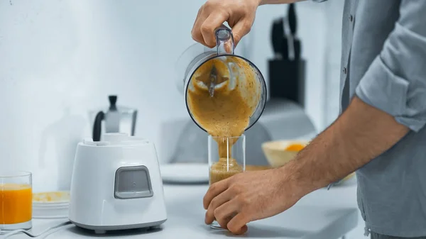 Ausgeschnittene Ansicht eines Mannes, der in der Küche frischen Smoothie ins Glas gießt — Stockfoto