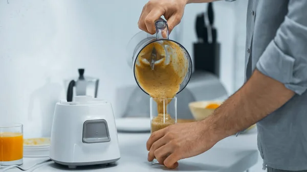 Vue recadrée de l'homme versant smoothie frais dans le verre dans la cuisine — Photo de stock