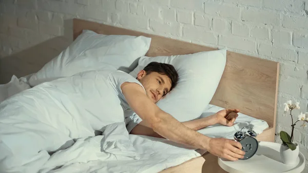 Aufgeweckter Mann schaltet Wecker aus, während er im Bett liegt — Stockfoto