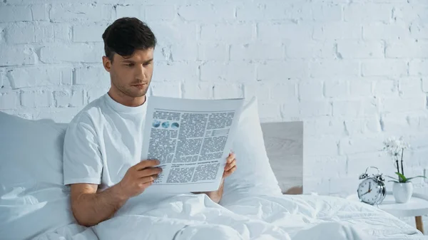 Чоловік сидить у ліжку і читає ранкову газету — стокове фото