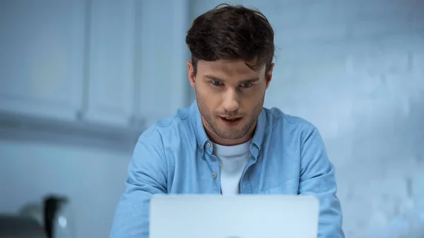 Pigiste concentré en chemise bleue travaillant sur ordinateur portable dans la cuisine — Photo de stock