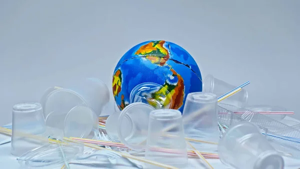 Globo vicino bicchieri di plastica e rifiuti su grigio, concetto ambientale — Foto stock