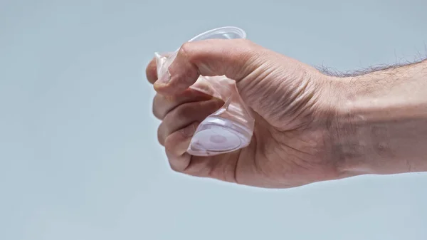 Vista recortada de hombre arrugando taza de plástico aislado en gris, concepto ambiental - foto de stock