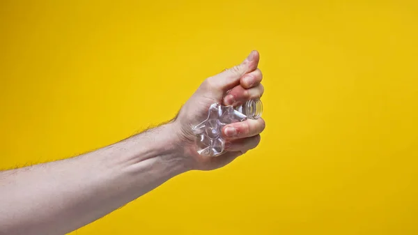 Vista recortada de hombre arrugando botella de plástico aislado en amarillo, cero concepto de residuos - foto de stock