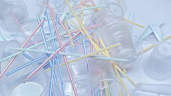 Vista de alto ângulo de copos de plástico perto de garfos e palhas coloridas em branco — Fotografia de Stock