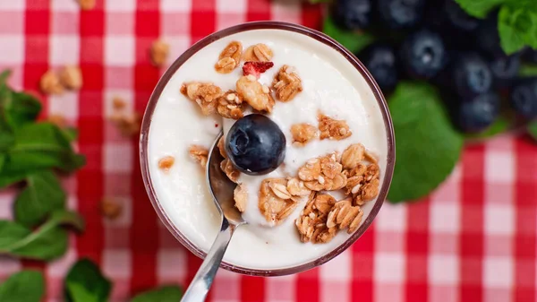 Vista superior de arándanos y granola en la parte superior de yogur fresco en vidrio con cuchara - foto de stock