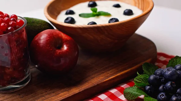 Свіжі фрукти, м'ята та ягоди біля дерев'яної миски з йогуртом на білому — стокове фото