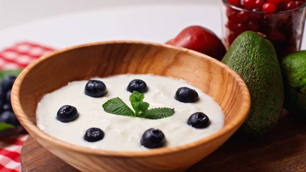 Fresh fruits near wooden bowl with yogurt and blueberries on white — Stock Photo