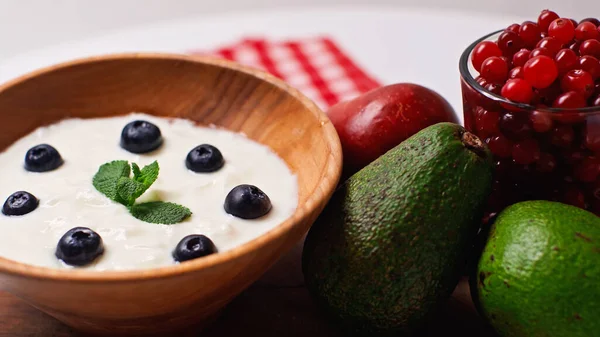 Фрукты рядом с деревянной миской с йогуртом и черникой на белом — Stock Photo