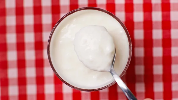 Top view of spoon near bowl with fresh yogurt on checkered background — Stock Photo