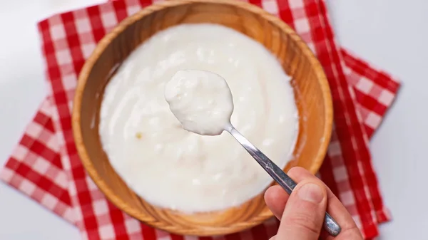 Vista superior del hombre sosteniendo cuchara con yogur cerca de un tazón borroso en una servilleta de tela a cuadros aislada en blanco - foto de stock