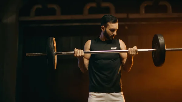 Athletic man training with barbell on dark background — Stock Photo