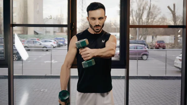 Sportivo muscolare che distoglie lo sguardo mentre si allena con i manubri in palestra — Foto stock