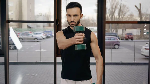 Muscular sportsman holding dumbbell while working out in gym — Stock Photo