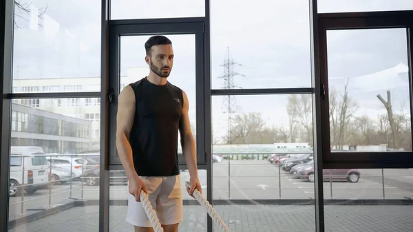 Athletic sportsman holding battle rope in gym — Stock Photo