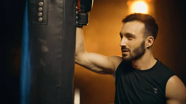 Boxer en gant regardant sac de boxe sur fond sombre — Photo de stock