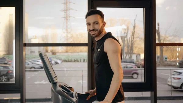 Усміхнений спортсмен дивиться на камеру під час тренувань на біговій доріжці в спортзалі — стокове фото