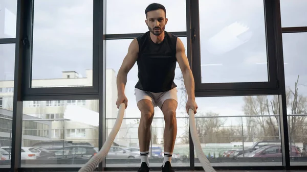 Allenamento sportivo con corda da battaglia e guardando la fotocamera in palestra — Foto stock