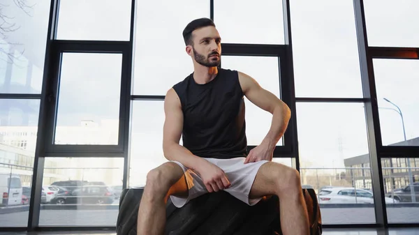 Bearded sportsman sitting on tire in gym — Stock Photo