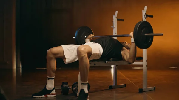 Athletic sportsman working out with barbell on dark background — Stock Photo