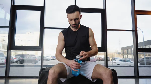 Спортсмен тримає спортивну пляшку, сидячи на шині в спортзалі — стокове фото