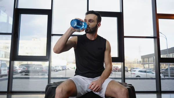 Спортсмен п'є воду, сидячи на шині в спортзалі — стокове фото