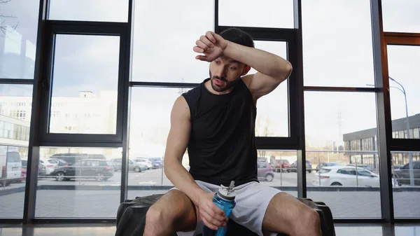 Müder Sportler hält Sportflasche in Turnhalle auf Reifen — Stockfoto