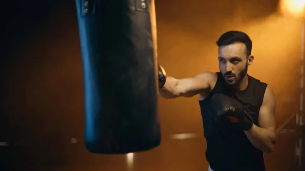 Sportsman training with punch bag on dark background — Stock Photo