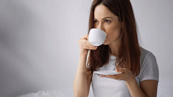 Bruna donna bere caffè da tazza bianca al mattino su sfondo grigio — Foto stock