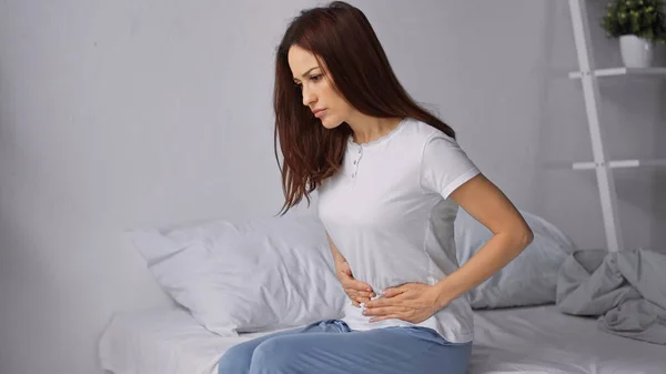 Morena mujer tocando vientre mientras siente dolor abdominal en el dormitorio - foto de stock
