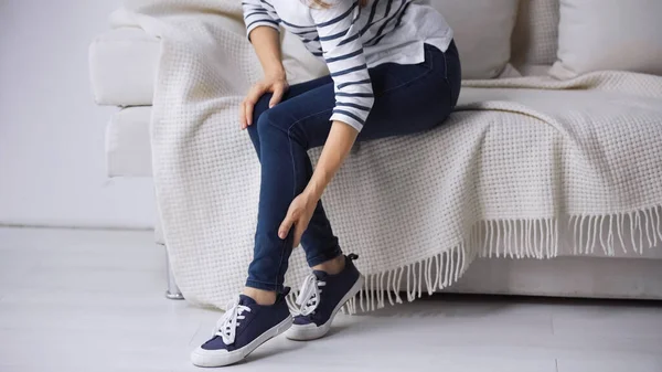 Partial view of woman sitting on couch and touching painful leg — Stock Photo