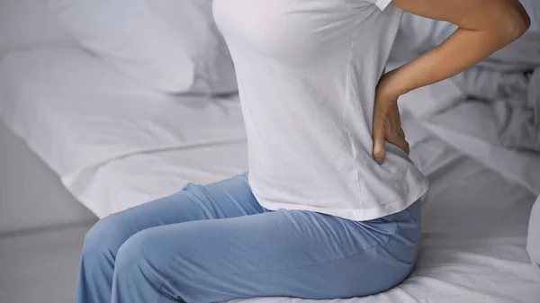 Cropped view of woman in pajamas sitting on bed and suffering from hurt in back — Stock Photo