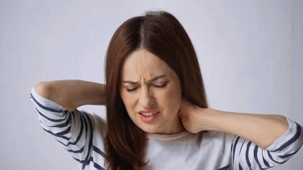 Brunette woman with closed eyes touching neck and frowning from pain on grey background — Stock Photo