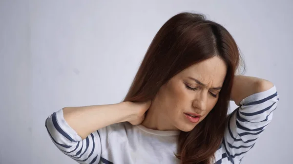 Unhappy woman touching painful neck and frowning with closed eyes on grey background — Stock Photo