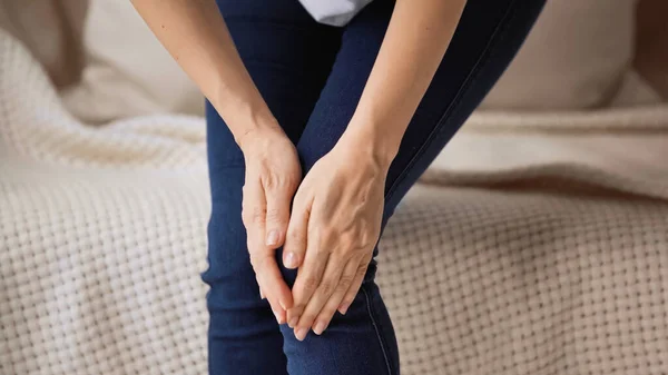 Vista ritagliata di donna toccando ginocchio doloroso mentre in piedi a casa — Foto stock