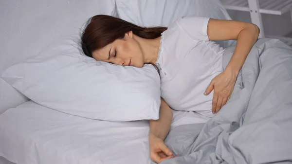 Brunette woman feeling pain in stomach while lying on bed — Stock Photo