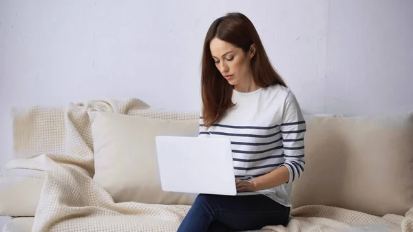 Femme brune assise sur le canapé à la maison et travaillant sur ordinateur portable — Photo de stock