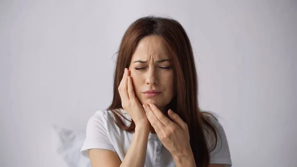 Donna infelice con mal di denti guancia toccante e accigliato con gli occhi chiusi su sfondo grigio — Foto stock