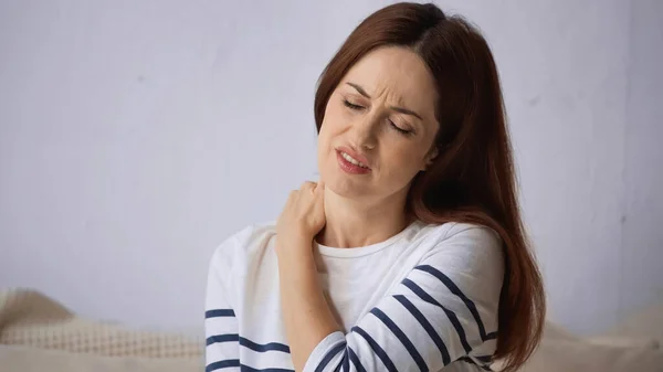 Morena mujer frunciendo el ceño con los ojos cerrados mientras sufre de dolor de cuello - foto de stock