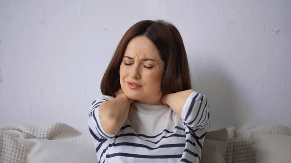 Frowning woman sitting on couch and touching painful neck — Stock Photo